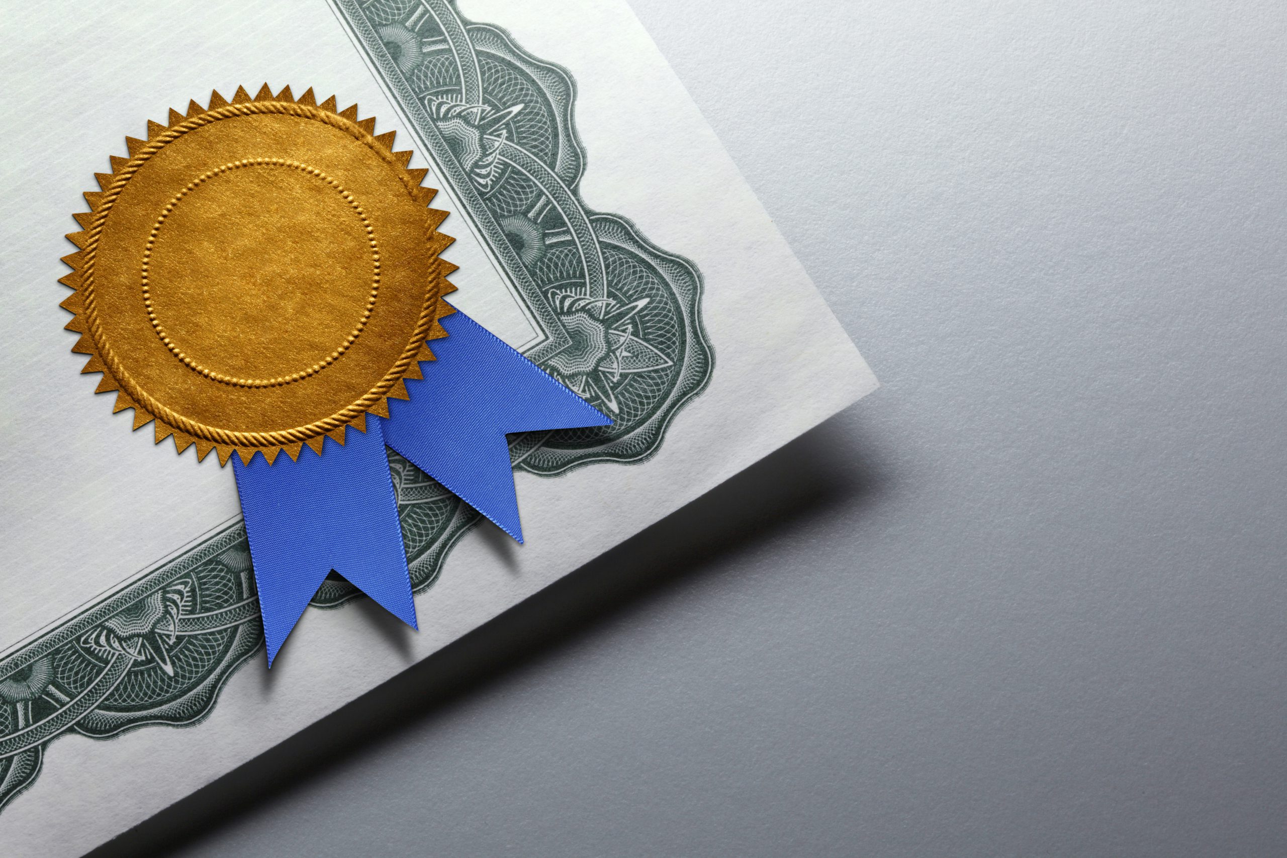 "A close-up of an official certificate with a gold embossed seal and blue ribbon, symbolizing achievement, quality, and accreditation."