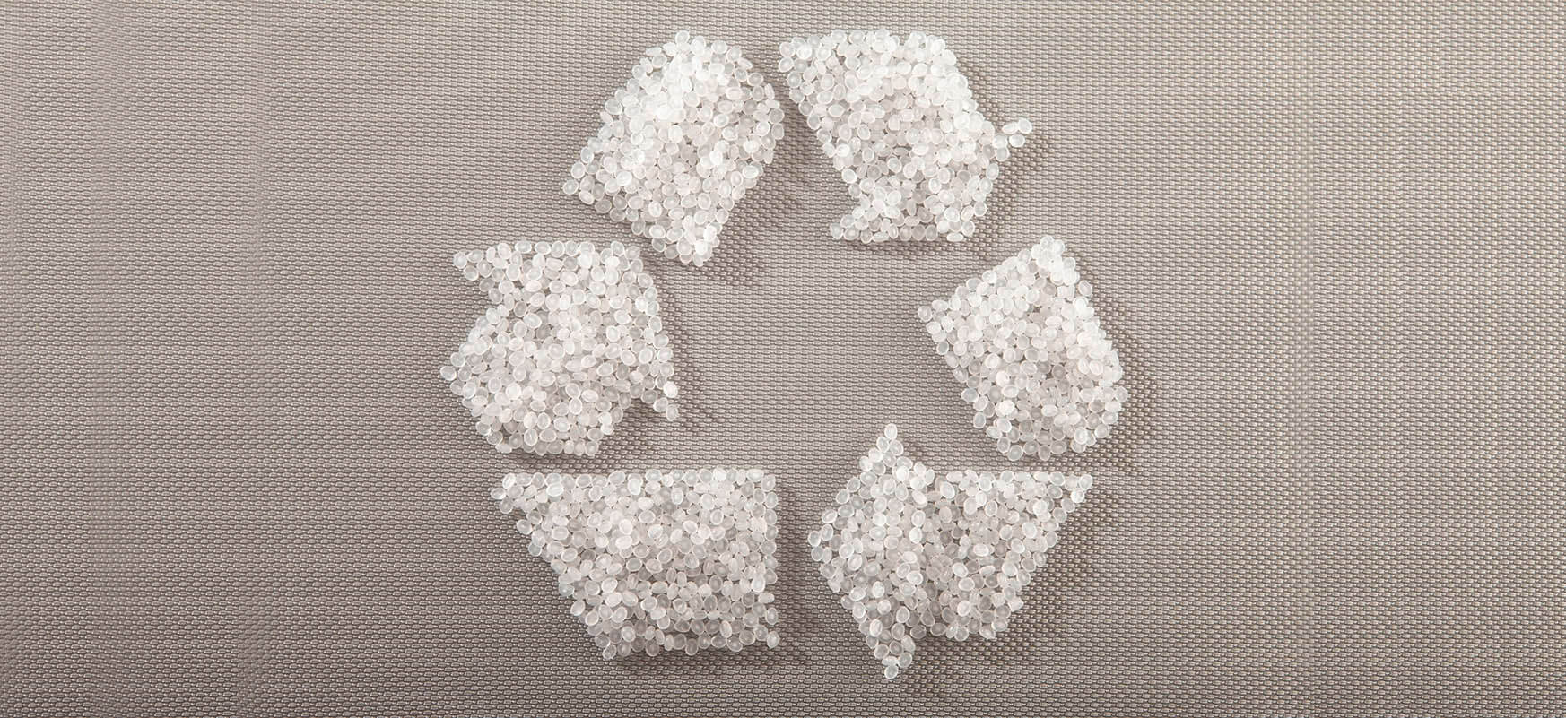 "Recycling symbol made of white plastic pellets on a textured gray background, representing sustainable plastic reuse and eco-friendly manufacturing."